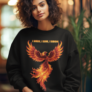 A young woman, possibly of Caucasian descent, with light brown hair pulled back, wearing a black PodLyft Phoenix Reign sweatshirt. The sweatshirt features a graphic of a stylized, fiery phoenix with the text "I BURN I RISE I REIGN" below it. She is looking directly at the camera with a confident expression, standing against a plain light grey background.