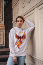 A young woman, possibly of Caucasian descent, with light brown hair pulled back, wearing a lavender PodLyft Phoenix Reign sweatshirt. The sweatshirt features a graphic of a stylized, fiery phoenix with the text "I BURN I RISE I REIGN" below it. She is looking directly at the camera with a confident expression, standing against a plain light grey background.