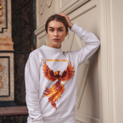 A young woman, possibly of Caucasian descent, with light brown hair pulled back, wearing a lavender PodLyft Phoenix Reign sweatshirt. The sweatshirt features a graphic of a stylized, fiery phoenix with the text "I BURN I RISE I REIGN" below it. She is looking directly at the camera with a confident expression, standing against a plain light grey background.