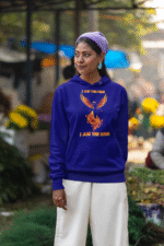 A young woman, possibly of Caucasian descent, with light brown hair pulled back, wearing a navy blue PodLyft Women's Revolution Hoodie. The hoodie features a graphic of a stylized, strong female figure, with the text "I AM THE FIRE I AM THE REVOLUTION" below it. She is looking directly at the camera with a confident expression, standing against a plain light grey background.