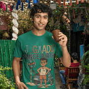 A young man, possibly of Caucasian descent, with short dark hair and a beard, wearing a bottle green PodLyft Men's Jugaadu t-shirt. The t-shirt features a graphic with the text "JUGAADU SINCE BIRTH." He is looking directly at the camera with a confident expression, standing against a plain light grey background.