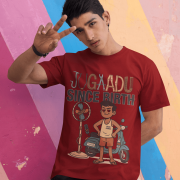 A young man, possibly of Caucasian descent, with short dark hair and a beard, wearing a maroon PodLyft Men's Jugaadu t-shirt. The t-shirt features a graphic with the text "JUGAADU SINCE BIRTH." He is looking directly at the camera with a confident expression, standing against a plain light grey background.