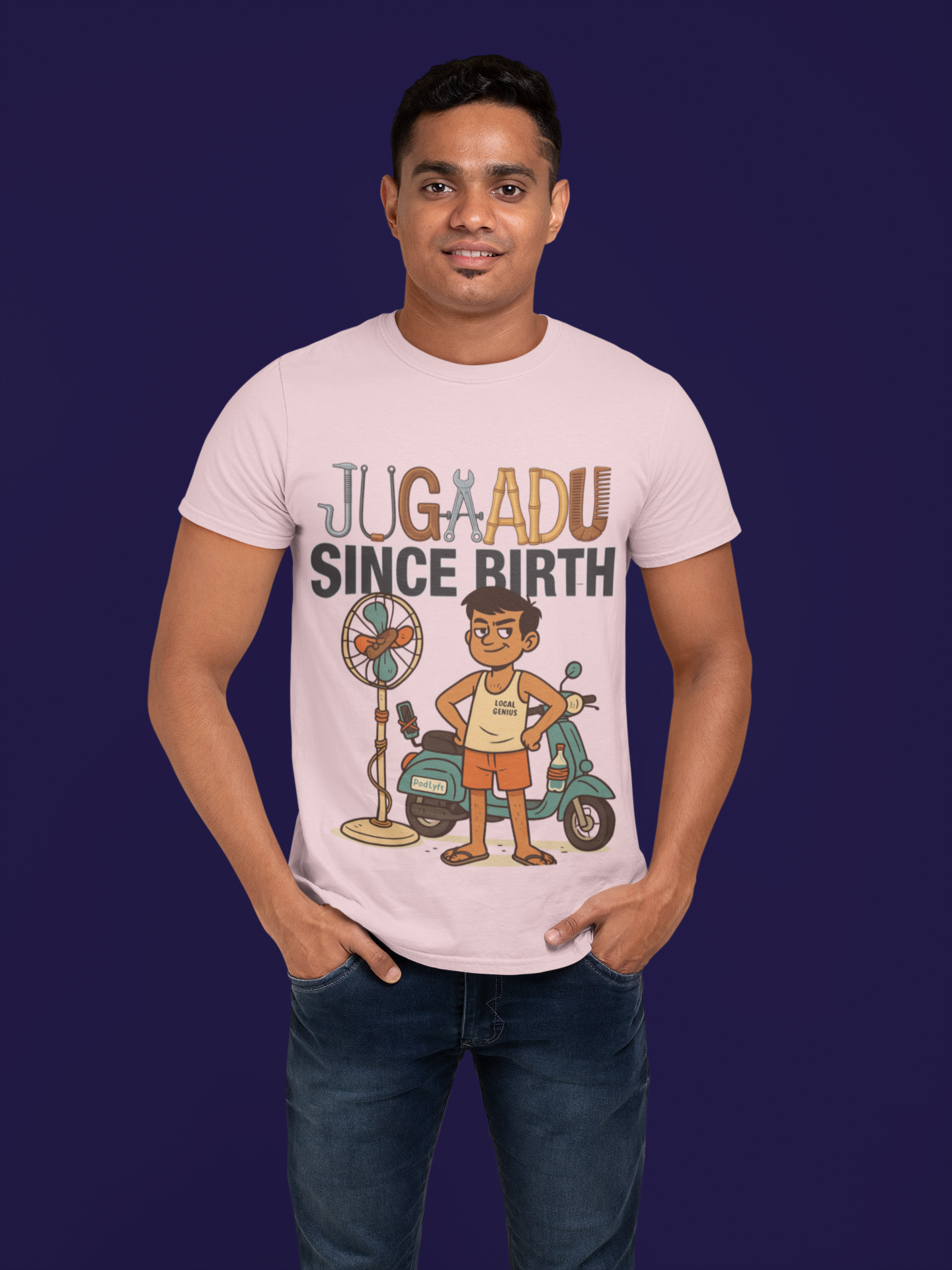 A young man, possibly of Caucasian descent, with short dark hair and a beard, wearing a light grayish orange PodLyft Men's Jugaadu t-shirt. The t-shirt features a graphic with the word "JUGAADU SINCE BIRTH." He is looking directly at the camera with a confident expression, standing against a plain light grey background.