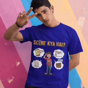 A young man, possibly of Caucasian descent, with short dark hair and a beard, wearing a navy blue t-shirt. The t-shirt features a humorous graphic with the Hindi text "SCENE KYA HAI" and a stylized question mark. He is looking directly at the camera with a confident expression, standing against a plain light grey background.