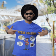 A young man, possibly of Caucasian descent, with short dark hair and a beard, wearing a royal blue t-shirt. The t-shirt features a humorous graphic with the Hindi text "SCENE KYA HAI" and a stylized question mark. He is looking directly at the camera with a confident expression, standing against a plain light grey background.