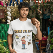 A young man, possibly of Caucasian descent, with short dark hair and a beard, wearing a white t-shirt. The t-shirt features a humorous graphic with the Hindi text "SCENE KYA HAI" and a stylized question mark. He is looking directly at the camera with a confident expression, standing against a plain light grey background.