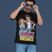 A young man, possibly of Caucasian descent, with short dark hair and a beard, wearing a black PodLyft Pataka t-shirt. The t-shirt features a flirty graphic with the text, "Girl, were you born on Diwali? Because You are PATAKA." He is looking directly at the camera with a confident expression, standing against a plain light grey background.