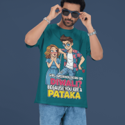 A young man, possibly of Caucasian descent, with short dark hair and a beard, wearing a petrol blue PodLyft Pataka t-shirt. The t-shirt features a flirty graphic with the text, "Girl, were you born on Diwali? Because You are PATAKA." He is looking directly at the camera with a confident expression, standing against a plain light grey background.