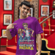A young man, possibly of Caucasian descent, with short dark hair and a beard, wearing a purple PodLyft Pataka t-shirt. The t-shirt features a flirty graphic with the text, "Girl, were you born on Diwali? Because You are PATAKA." He is looking directly at the camera with a confident expression, standing against a plain light grey background.