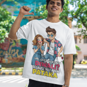 A young man, possibly of Caucasian descent, with short dark hair and a beard, wearing a white PodLyft Pataka t-shirt. The t-shirt features a flirty graphic with the text, "Girl, were you born on Diwali? Because You are PATAKA." He is looking directly at the camera with a confident expression, standing against a plain light grey background.