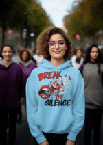 A young woman, possibly of Caucasian descent, with light brown hair pulled back, wearing a baby blue PodLyft Women's Break the Silence Hoodie. The hoodie features a graphic of a padlocked mouth with doves and butterflies bursting out, and the text "BREAK THE SILENCE" and "RAISE YOUR VOICE." She is looking directly at the camera with a confident expression, standing against a plain light grey background.
