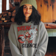 A young woman, possibly of Caucasian descent, with light brown hair pulled back, wearing a grey PodLyft Women's Break the Silence Hoodie. The hoodie features a graphic of a padlocked mouth with doves and butterflies bursting out, and the text "BREAK THE SILENCE" and "RAISE YOUR VOICE." She is looking directly at the camera with a confident expression, standing against a plain light grey background.
