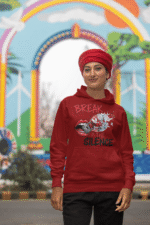 A young woman, possibly of Caucasian descent, with light brown hair pulled back, wearing a maroon PodLyft Women's Break the Silence Hoodie. The hoodie features a graphic of a padlocked mouth with doves and butterflies bursting out, and the text "BREAK THE SILENCE" and "RAISE YOUR VOICE." She is looking directly at the camera with a confident expression, standing against a plain light grey background.