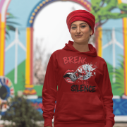 A young woman, possibly of Caucasian descent, with light brown hair pulled back, wearing a maroon PodLyft Women's Break the Silence Hoodie. The hoodie features a graphic of a padlocked mouth with doves and butterflies bursting out, and the text "BREAK THE SILENCE" and "RAISE YOUR VOICE." She is looking directly at the camera with a confident expression, standing against a plain light grey background.