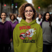 A young woman, possibly of Caucasian descent, with light brown hair pulled back, wearing an olive green PodLyft Women's Break the Silence Hoodie. The hoodie features a graphic of a padlocked mouth with doves and butterflies bursting out, and the text "BREAK THE SILENCE" and "RAISE YOUR VOICE." She is looking directly at the camera with a confident expression, standing against a plain light grey background.