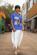 A woman smiling while wearing a royal blue PodLyft Girls Savage Queen Tee and white traditional Indian clothing. She is standing on a city street. The graphic features a woman giving a thumbs-up, with text bubbles that translate to "If a guy proposes to me, I reject him" and "But I salute his choice.