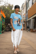 A woman smiling while wearing a sky blue PodLyft Girls Savage Queen Tee and white traditional Indian clothing. She is standing on a city street. The graphic features a woman giving a thumbs-up, with text bubbles that translate to "If a guy proposes to me, I reject him" and "But I salute his choice.