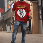 A young man, possibly of Caucasian descent, with short dark hair and a beard, wearing a maroon PodLyft Men's Bollywood Swag T-shirt. The t-shirt features a graphic with a funny movie dialogue. He is looking directly at the camera with a confident expression, standing against a plain light grey background.