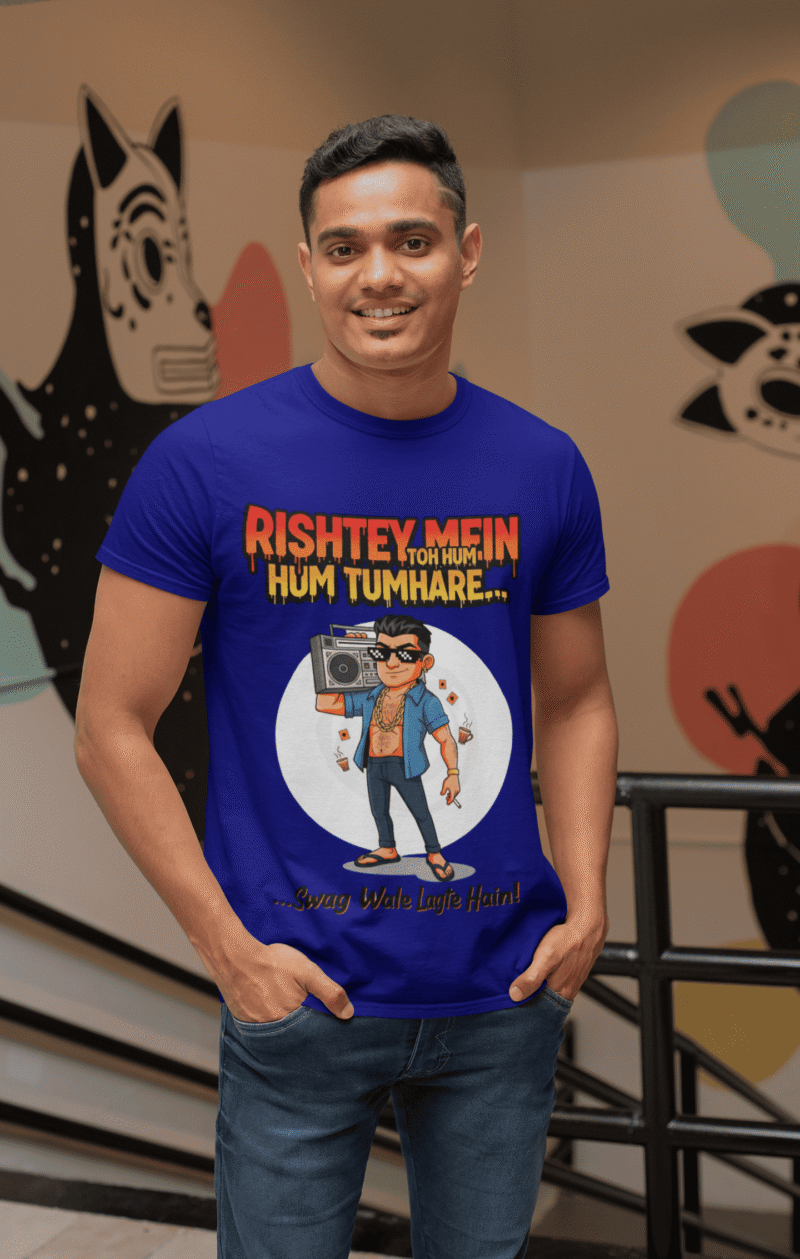 A young man, possibly of Caucasian descent, with short dark hair and a beard, wearing a navy blue PodLyft Men's Bollywood Swag T-shirt. The t-shirt features a graphic with a funny movie dialogue. He is looking directly at the camera with a confident expression, standing against a plain light grey background.