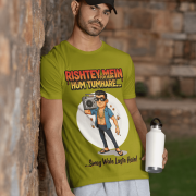 A young man, possibly of Caucasian descent, with short dark hair and a beard, wearing an olive green PodLyft Men's Bollywood Swag T-shirt. The t-shirt features a graphic with a funny movie dialogue. He is looking directly at the camera with a confident expression, standing against a plain light grey background.