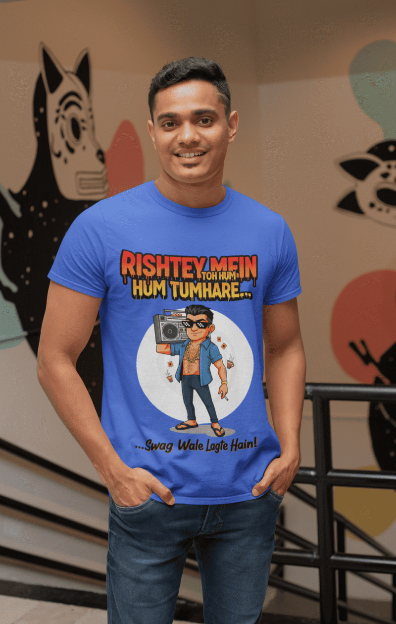 A young man, possibly of Caucasian descent, with short dark hair and a beard, wearing a royal blue PodLyft Men's Bollywood Swag T-shirt. The t-shirt features a graphic with a funny movie dialogue. He is looking directly at the camera with a confident expression, standing against a plain light grey background.