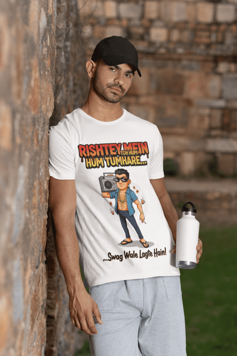 A young man, possibly of Caucasian descent, with short dark hair and a beard, wearing a white PodLyft Men's Bollywood Swag T-shirt. The t-shirt features a graphic with a funny movie dialogue. He is looking directly at the camera with a confident expression, standing against a plain light grey background.