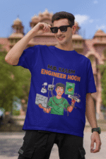A man wearing a navy blue PodLyft Men's Engineering Stress Tee while holding his sunglasses up on a sunny day. He is standing outdoors with a large, classical building in the background. The graphic on the shirt shows a stressed-out male engineer surrounded by broken electronics, wires, and coffee, with the Hindi text "MAA KASAM ENGINEER HOON" and a book titled "LEARN PYTHON 7 DAYS!
