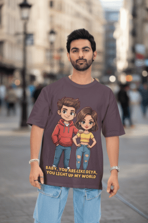 A young man with short dark hair and a beard, wearing a black PodLyft oversized Light Up T-shirt. The t-shirt features a graphic of a cartoon-style couple and the flirty text, "Baby You Are Like Diya, You Light Up My World." He is looking directly at the camera with a confident expression, standing against a plain light grey background.