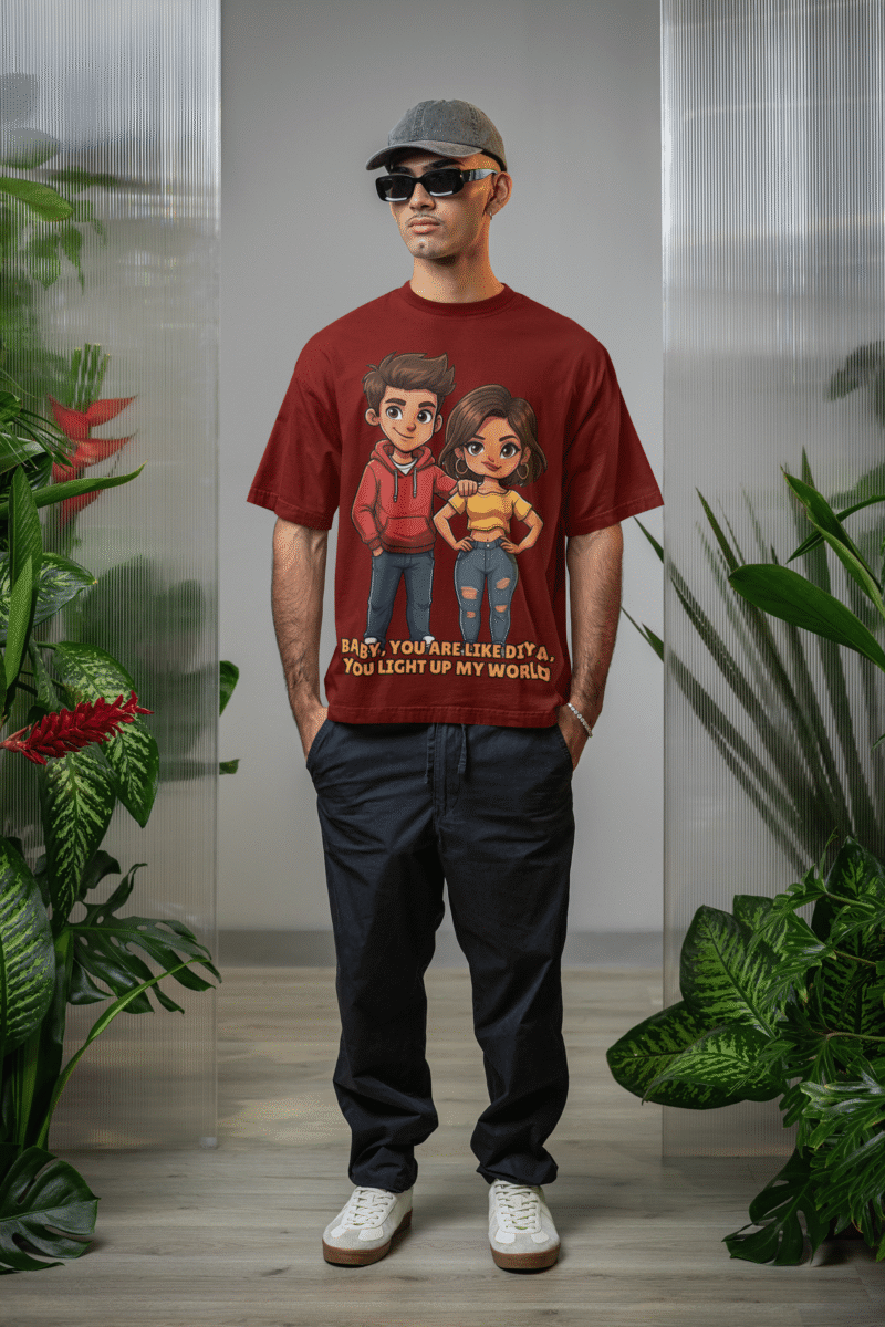 young man, possibly of Caucasian descent, with short dark hair and a beard, wearing a maroon PodLyft oversized Light Up T-shirt. The t-shirt features a graphic of a cartoon-style couple and the flirty text, "Baby You Are Like Diya, You Light Up My World." He is looking directly at the camera with a confident expression, standing against a plain light grey background.