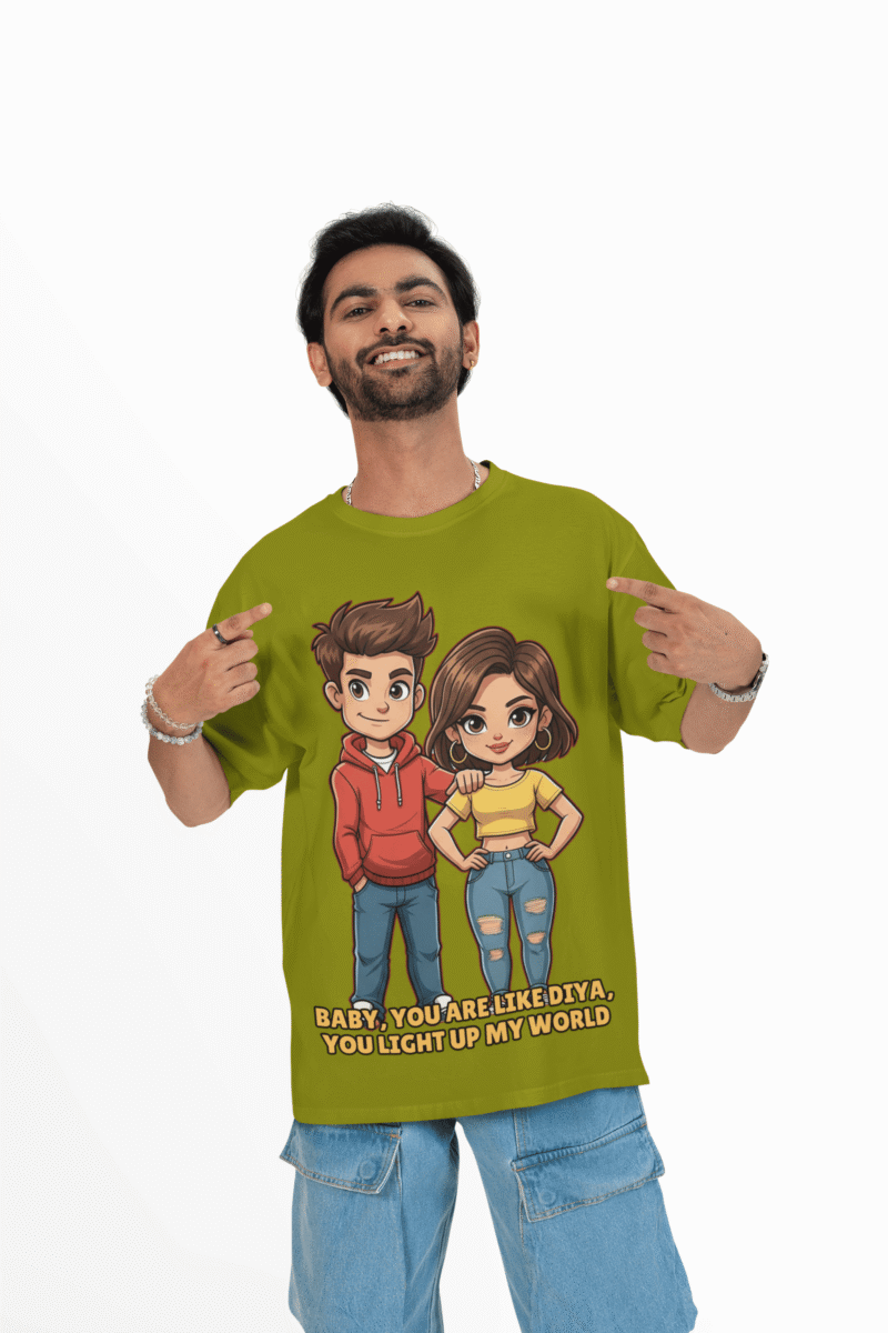 A young man, possibly of Caucasian descent, with short dark hair and a beard, wearing an olive green PodLyft oversized Light Up T-shirt. The t-shirt features a graphic of a cartoon-style couple and the flirty text, "Baby You Are Like Diya, You Light Up My World." He is looking directly at the camera with a confident expression, standing against a plain light grey background.