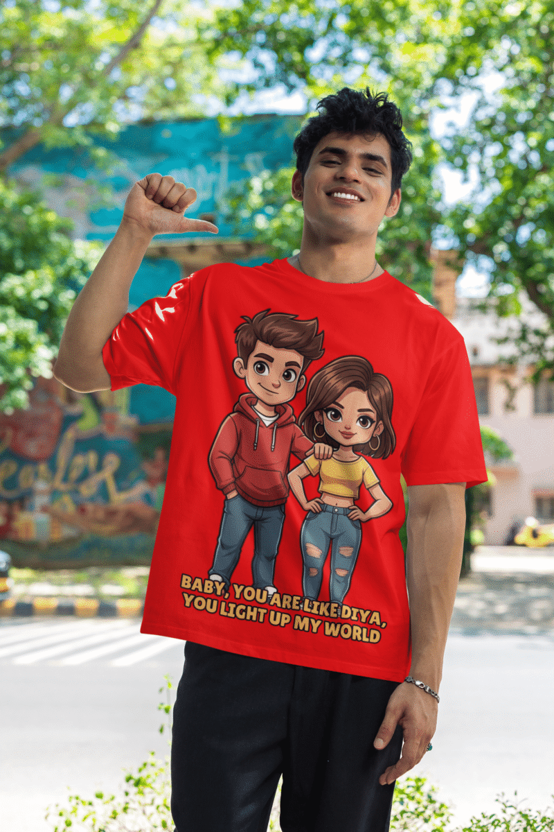 A young man, possibly of Caucasian descent, with short dark hair and a beard, wearing a red PodLyft oversized Light Up T-shirt. The t-shirt features a graphic of a cartoon-style couple and the flirty text, "Baby You Are Like Diya, You Light Up My World." He is looking directly at the camera with a confident expression, standing against a plain light grey background.