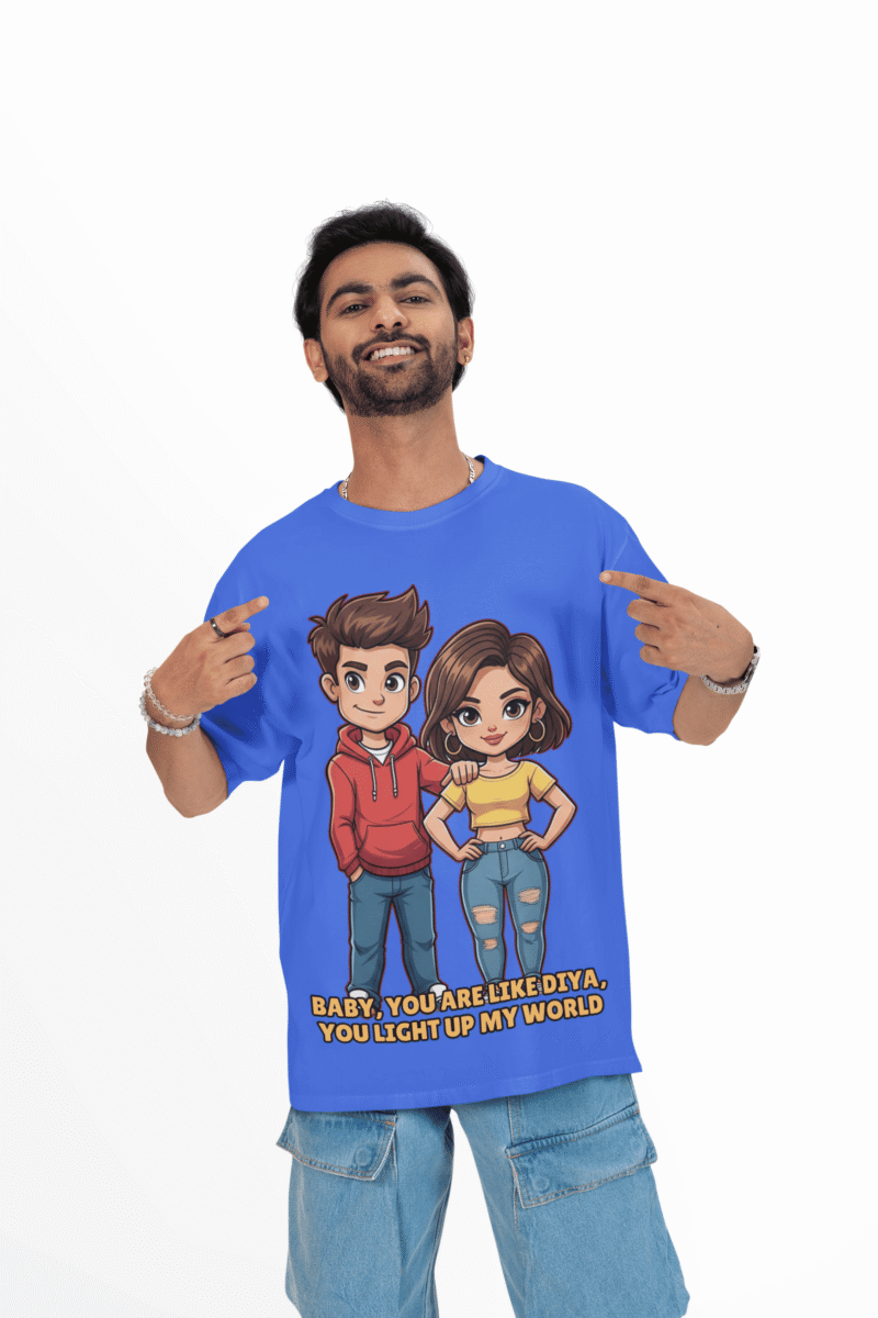 A young man, possibly of Caucasian descent, with short dark hair and a beard, wearing a royal blue PodLyft oversized Light Up T-shirt. The t-shirt features a graphic of a cartoon-style couple and the flirty text, "Baby You Are Like Diya, You Light Up My World." He is looking directly at the camera with a confident expression, standing against a plain light grey background.