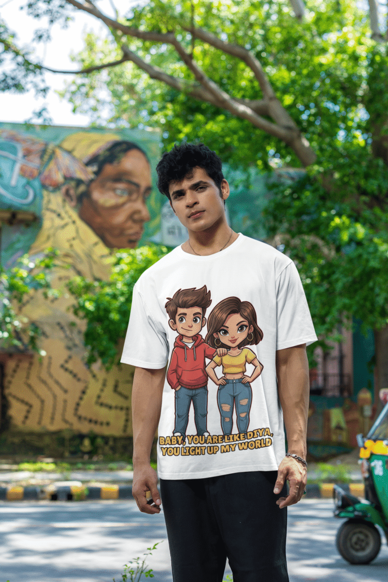 A young man, possibly of Caucasian descent, with short dark hair and a beard, wearing a white PodLyft oversized Light Up T-shirt. The t-shirt features a graphic of a cartoon-style couple and the flirty text, "Baby You Are Like Diya, You Light Up My World." He is looking directly at the camera with a confident expression, standing against a plain light grey background.