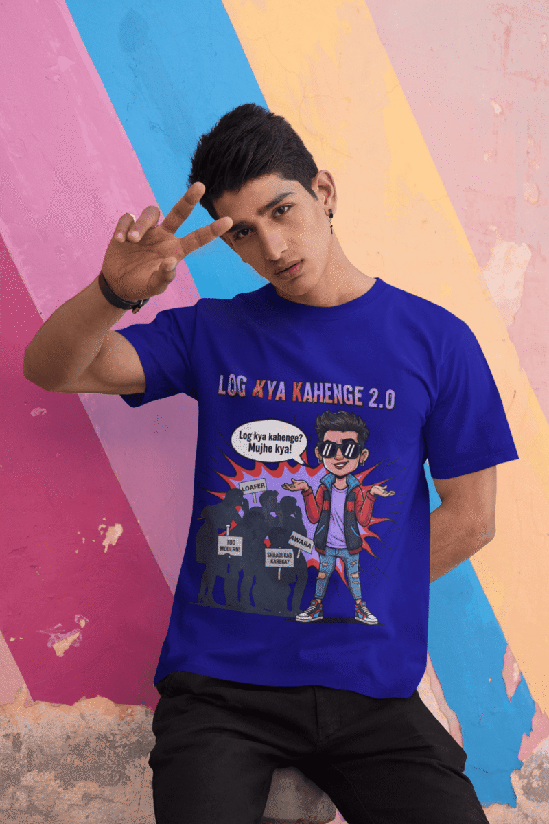 A young man, possibly of Caucasian descent, with short dark hair and a beard, wearing a navy blue PodLyft Log Kya Kahenge T-shirt. The t-shirt features a funny social parody graphic with Hindi text. He is looking directly at the camera with a confident expression, standing against a plain light grey background.