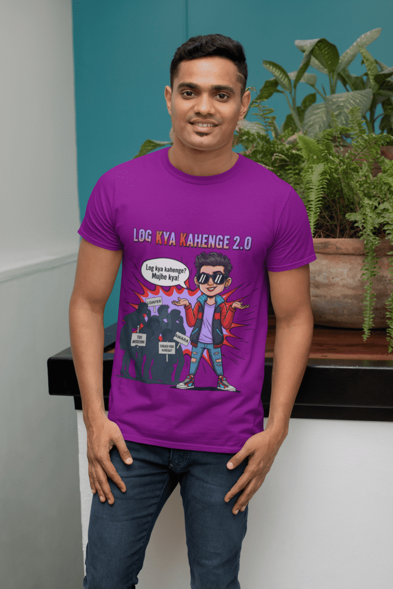 A young man, possibly of Caucasian descent, with short dark hair and a beard, wearing a purple PodLyft Log Kya Kahenge T-shirt. The t-shirt features a funny social parody graphic with Hindi text. He is looking directly at the camera with a confident expression, standing against a plain light grey background.