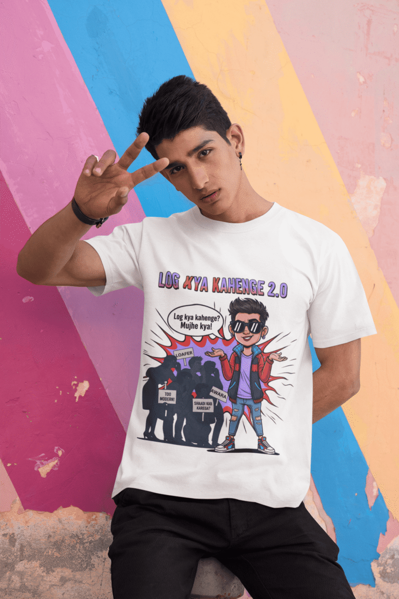 A young man, possibly of Caucasian descent, with short dark hair and a beard, wearing a white PodLyft Log Kya Kahenge T-shirt. The t-shirt features a funny social parody graphic with Hindi text. He is looking directly at the camera with a confident expression, standing against a plain light grey background.