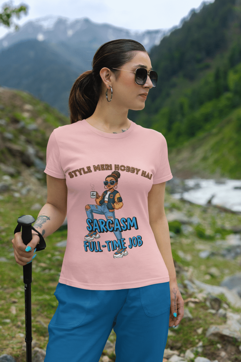 A woman wearing a baby pink PodLyft Women's Full-Time Sarcasm Tee indoors next to a pool table. The graphic features a stylized woman holding a coffee cup, with the text "STYLE MERI HOBBY HAI" and "SARCASM FULL-TIME JOB.