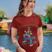 A woman wearing a maroon PodLyft Women's Full-Time Sarcasm Tee outdoors with a lake and mountains in the background. The graphic features a stylized woman holding a coffee cup, with the text "STYLE MERI HOBBY HAI" and "SARCASM FULL-TIME JOB.