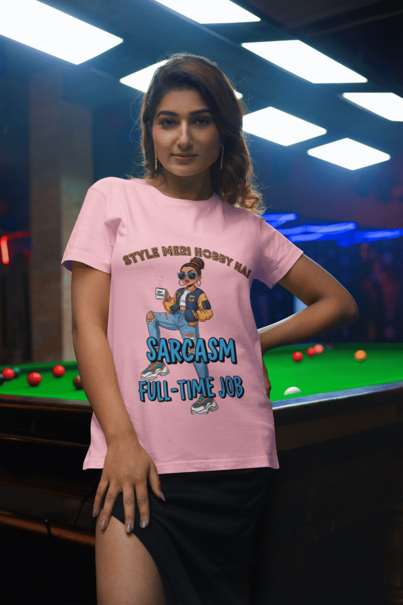 A woman wearing a light pink PodLyft Women's Full-Time Sarcasm Tee in a mountain setting, holding a hiking pole. The graphic features a stylized woman character holding a coffee cup, with the text "STYLE MERI HOBBY HAI" and "SARCASM FULL-TIME JOB.