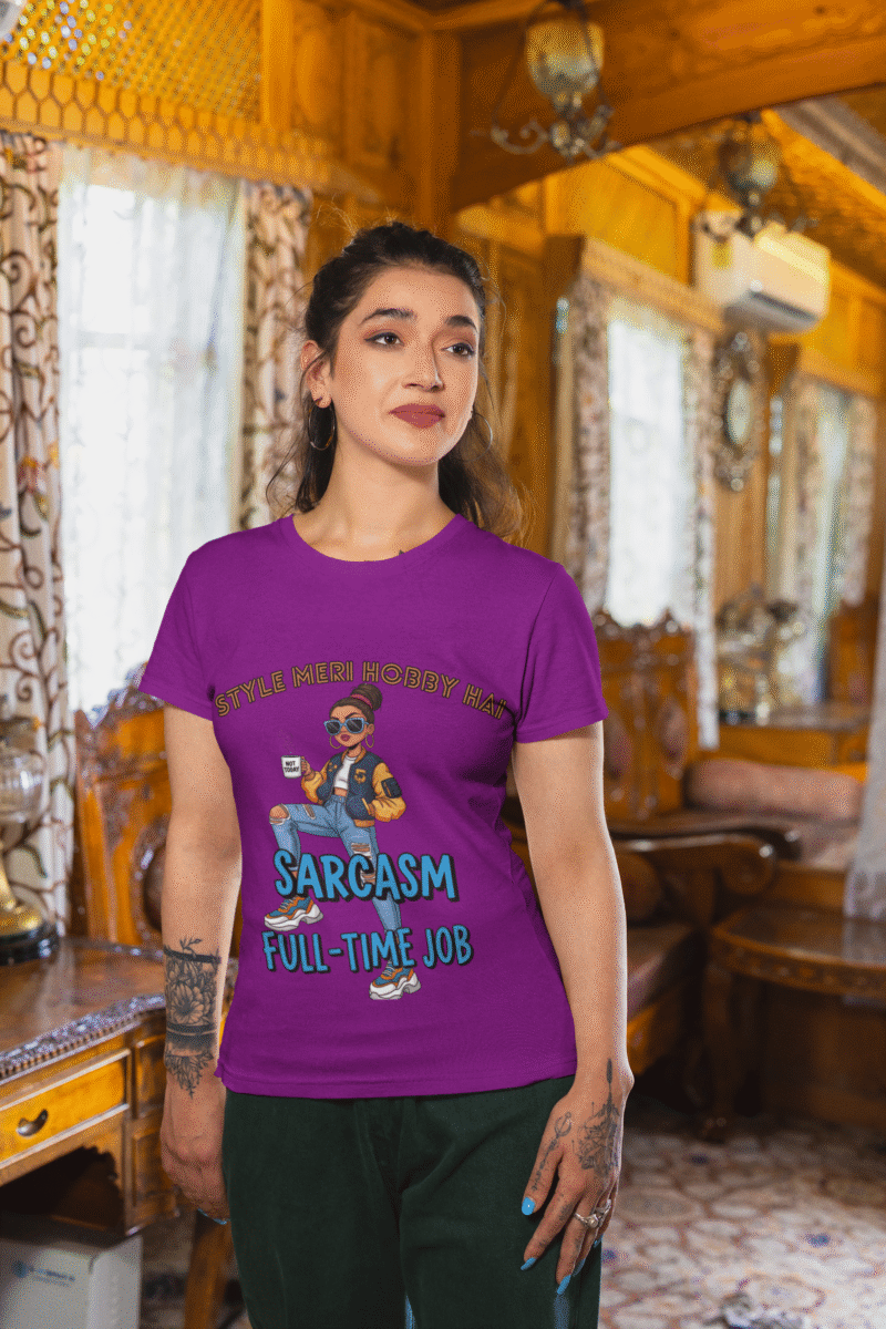 A woman wearing a purple PodLyft Women's Full-Time Sarcasm Tee in a cozy, wood-paneled room. The graphic features a stylized woman holding a coffee cup, with the text "STYLE MERI HOBBY HAI" and "SARCASM FULL-TIME JOB.