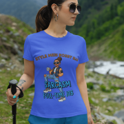 A woman wearing a royal blue PodLyft Women's Full-Time Sarcasm Tee in a mountain setting, holding a hiking pole. The graphic features a stylized woman holding a coffee cup, with the text "STYLE MERI HOBBY HAI" and "SARCASM FULL-TIME JOB.