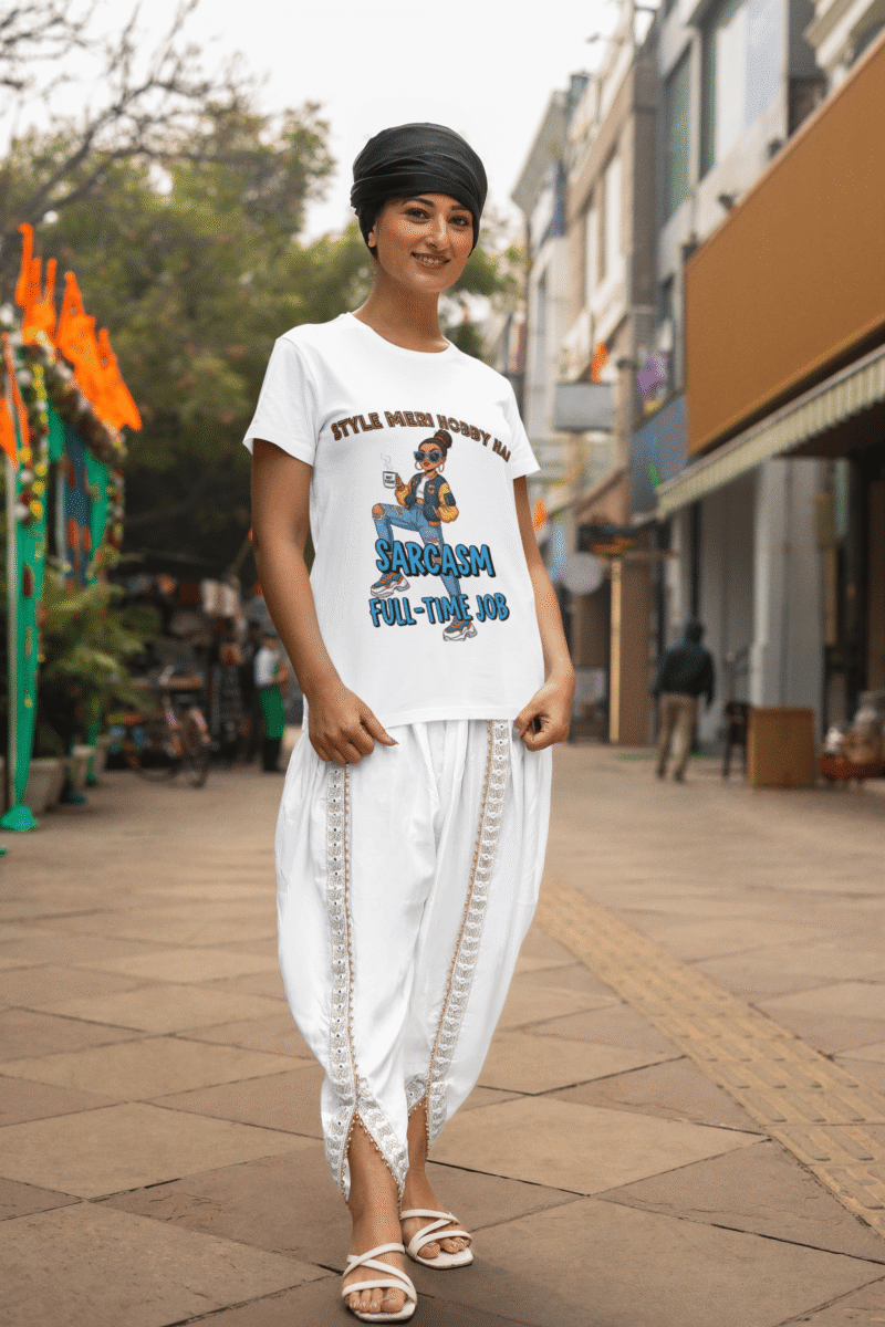 A woman smiling while wearing a white PodLyft Women's Full-Time Sarcasm Tee and white traditional Indian clothing. She is standing on a city street. The graphic shows a stylized woman holding a coffee cup, with the text "STYLE MERI HOBBY HAI" and "SARCASM FULL-TIME JOB.