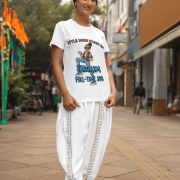 A woman smiling while wearing a white PodLyft Women's Full-Time Sarcasm Tee and white traditional Indian clothing. She is standing on a city street. The graphic shows a stylized woman holding a coffee cup, with the text "STYLE MERI HOBBY HAI" and "SARCASM FULL-TIME JOB.