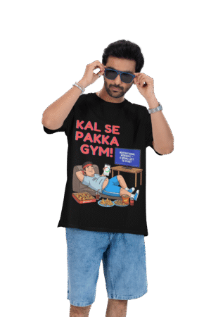 A man wearing a black PodLyft Men's Procrastinator Gym Tee against a solid dark green background, adjusting his blue sunglasses. The graphic shows a cartoon man relaxing on a couch surrounded by junk food, with the Hindi text "KAL SE PAKKA GYM!" and a TV screen saying "MOTIVATIONAL WORKOUT: 4 HOURS LEFT TO START.