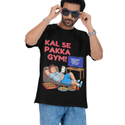 A man wearing a black PodLyft Men's Procrastinator Gym Tee against a solid dark green background, adjusting his blue sunglasses. The graphic shows a cartoon man relaxing on a couch surrounded by junk food, with the Hindi text "KAL SE PAKKA GYM!" and a TV screen saying "MOTIVATIONAL WORKOUT: 4 HOURS LEFT TO START.