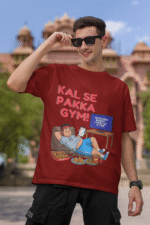 A man smiling and posing in a maroon PodLyft Men's Procrastinator Gym Tee outdoors with a wall mural in the background. The graphic shows a cartoon man relaxing on a couch surrounded by junk food, with the Hindi text "KAL SE PAKKA GYM!" and a TV screen saying "MOTIVATIONAL WORKOUT: 4 HOURS LEFT TO START.
