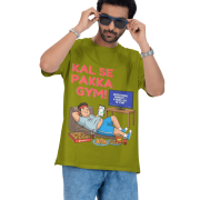 A man wearing an olive green PodLyft Men's Procrastinator Gym Tee against a solid dark green background, adjusting his blue sunglasses. The graphic shows a cartoon man relaxing on a couch surrounded by junk food, with the Hindi text "KAL SE PAKKA GYM!" (Definitely Gym From Tomorrow!) and a TV screen saying "MOTIVATIONAL WORKOUT: 4 HOURS LEFT TO START.