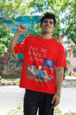 A man smiling and posing in a red PodLyft Men's Procrastinator Gym Tee outdoors with a wall mural in the background. The graphic shows a cartoon man relaxing on a couch surrounded by junk food, with the Hindi text "KAL SE PAKKA GYM!" and a TV screen saying "MOTIVATIONAL WORKOUT: 4 HOURS LEFT TO START.