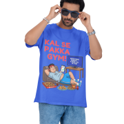 A man wearing a royal blue PodLyft Men's Procrastinator Gym Tee against a solid dark green background, adjusting his blue sunglasses. The graphic shows a cartoon man relaxing on a couch surrounded by junk food, with the Hindi text "KAL SE PAKKA GYM!" and a TV screen saying "MOTIVATIONAL WORKOUT: 4 HOURS LEFT TO START.