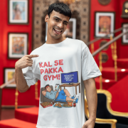 A man winking and pointing to his white PodLyft Men's Procrastinator Gym Tee in a room with a red wall and staircase. The graphic shows a cartoon man relaxing on a couch surrounded by junk food, with the Hindi text "KAL SE PAKKA GYM!" and a TV screen saying "MOTIVATIONAL WORKOUT: 4 HOURS LEFT TO START.
